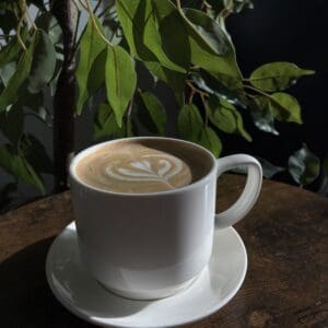 Coffee cup with latte art beside plant.